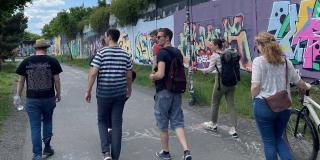 Ein paar Mitglieder laufen einen Weg entlang, im Hintergrund eine Wand mit Graffiti