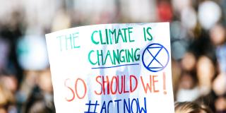 A photo taken at a pro-climate protest. The sign reads "The climate is changing, so should we! Act Now!"