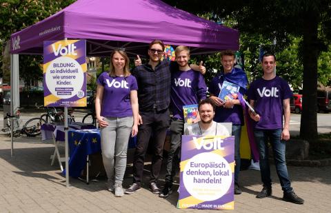 Mitglieder des Volt-Teams aus Heidelberg vor einem Pavillon, daneben Volt-Wahlplakate.